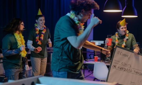 Group of coworkers celebrating a contest win with a giant check and party hats.